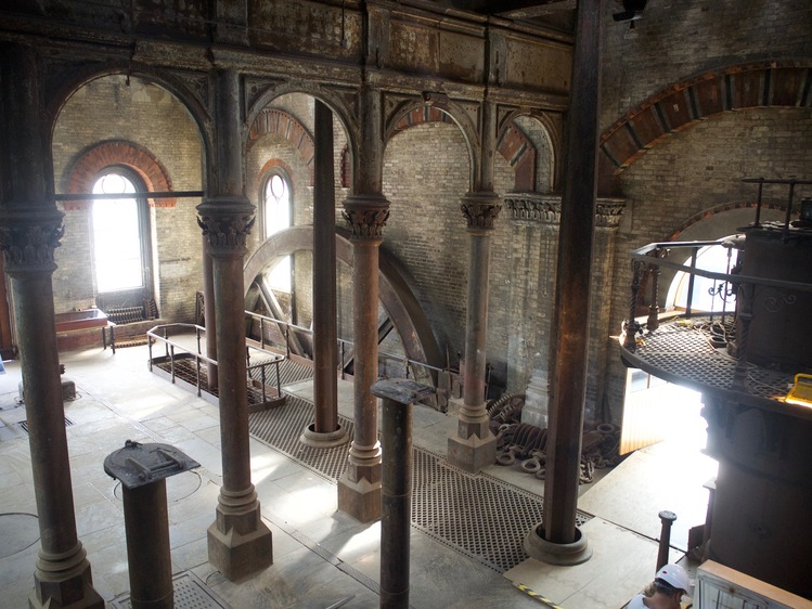 Looking down into a room with rusting metal pillars and a large metal wheel in the background.